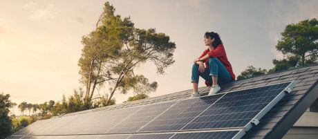 Frau sitzt auf einem Dach mit Solarpanels